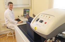 Arzt schaut auf Patienten, der auf Liege an einem Apparat liegt, Sportorthopäde der Uniklinik Rostock